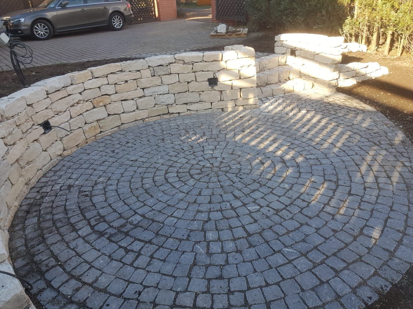 Kreisförmige Steinterrasse mit konzentrischer Pflasterung, umgeben von einer hellen Steinmauer und Stufen