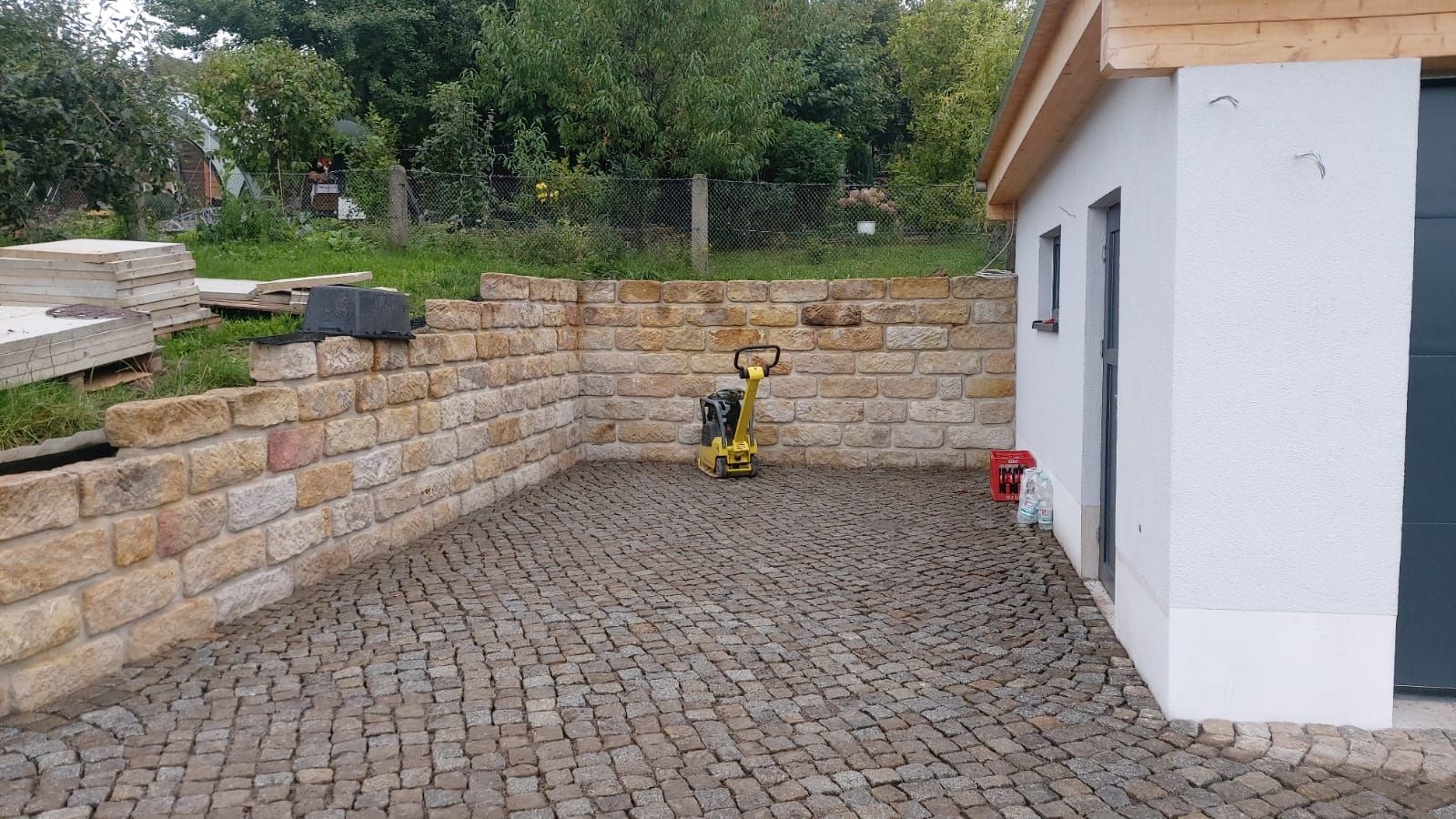 Gepflasterter Innenhof begrenzt durch eine Steinmauer und ein weißes Gebäude mit einer grauen Tür.