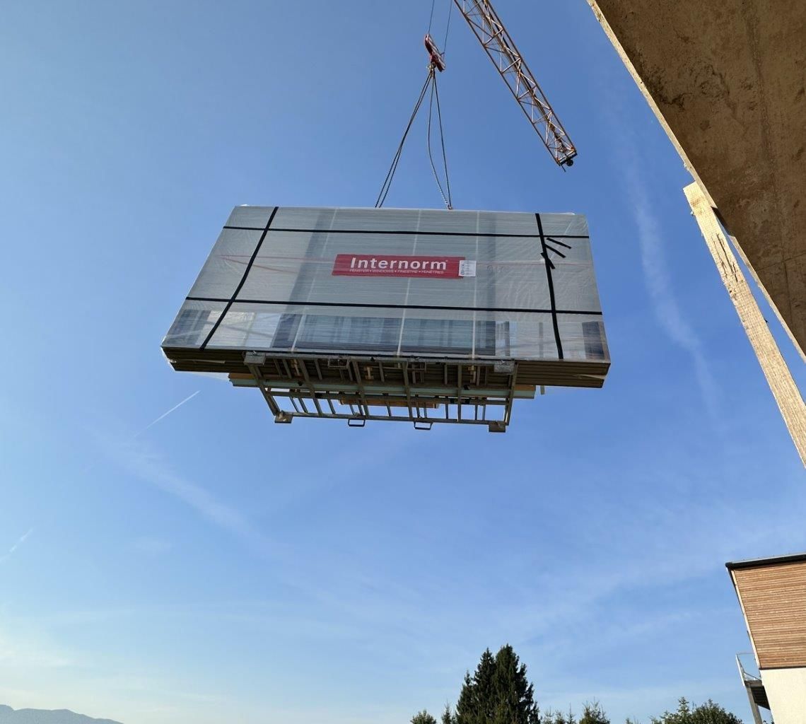 Ein Kran hebt einen großen, verpackten Container vor einem klaren blauen Himmel
