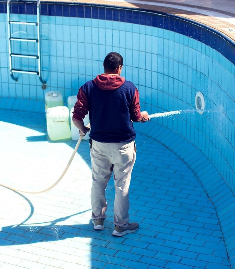 Un hombre está limpiando una piscina con una manguera.