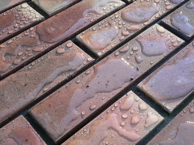 Tuiles de brique, motif en angle, humides de gouttelettes d'eau, diverses nuances brun-rougeâtre.