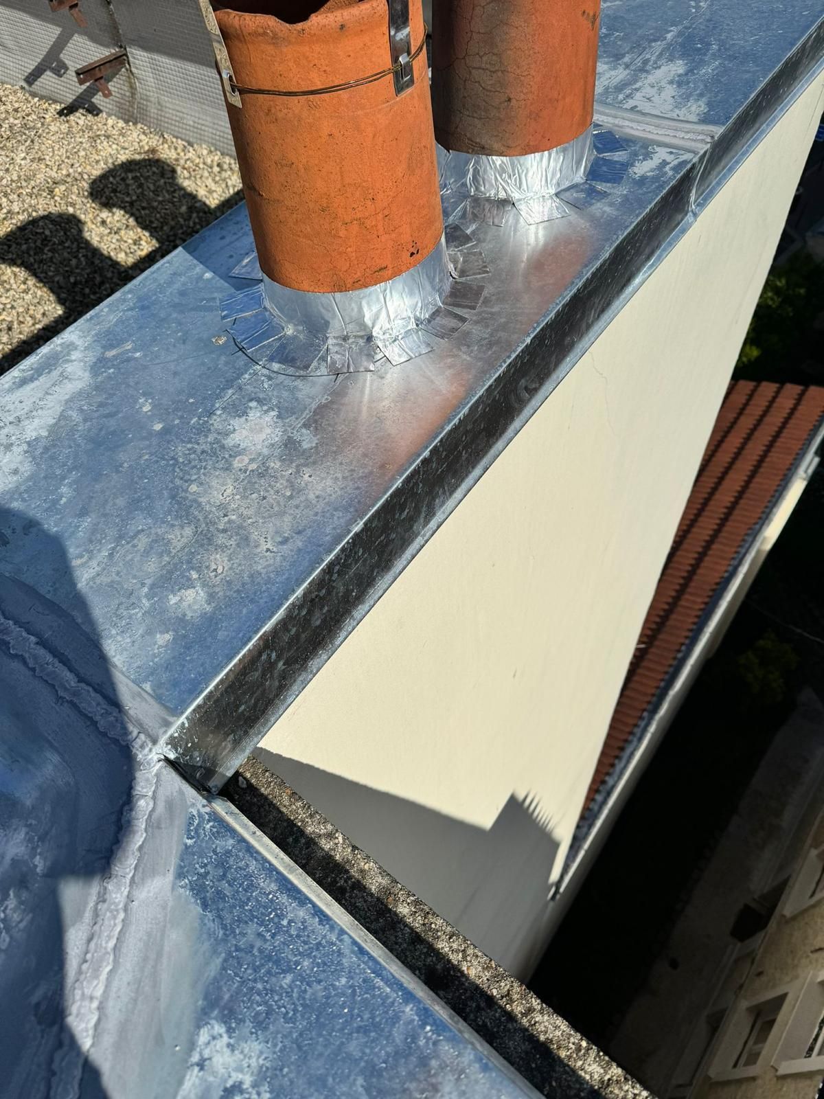 Gros plan sur une toiture métallique avec des souches de cheminée. La toiture présente une partie argentée et blanche avec une gouttière.