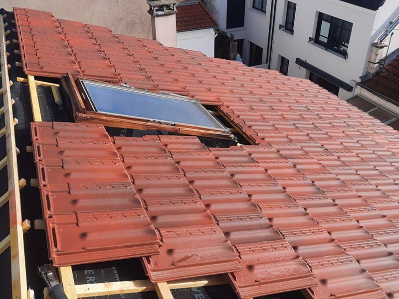 Toiture en construction avec tuiles rouges et puits de lumière.