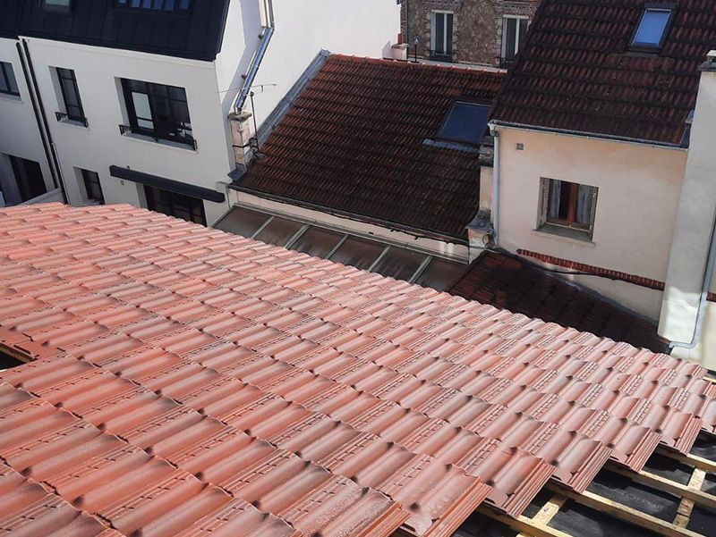 Pose de nouvelles tuiles en terre cuite orange sur un bâtiment, d'autres bâtiments en arrière-plan.
