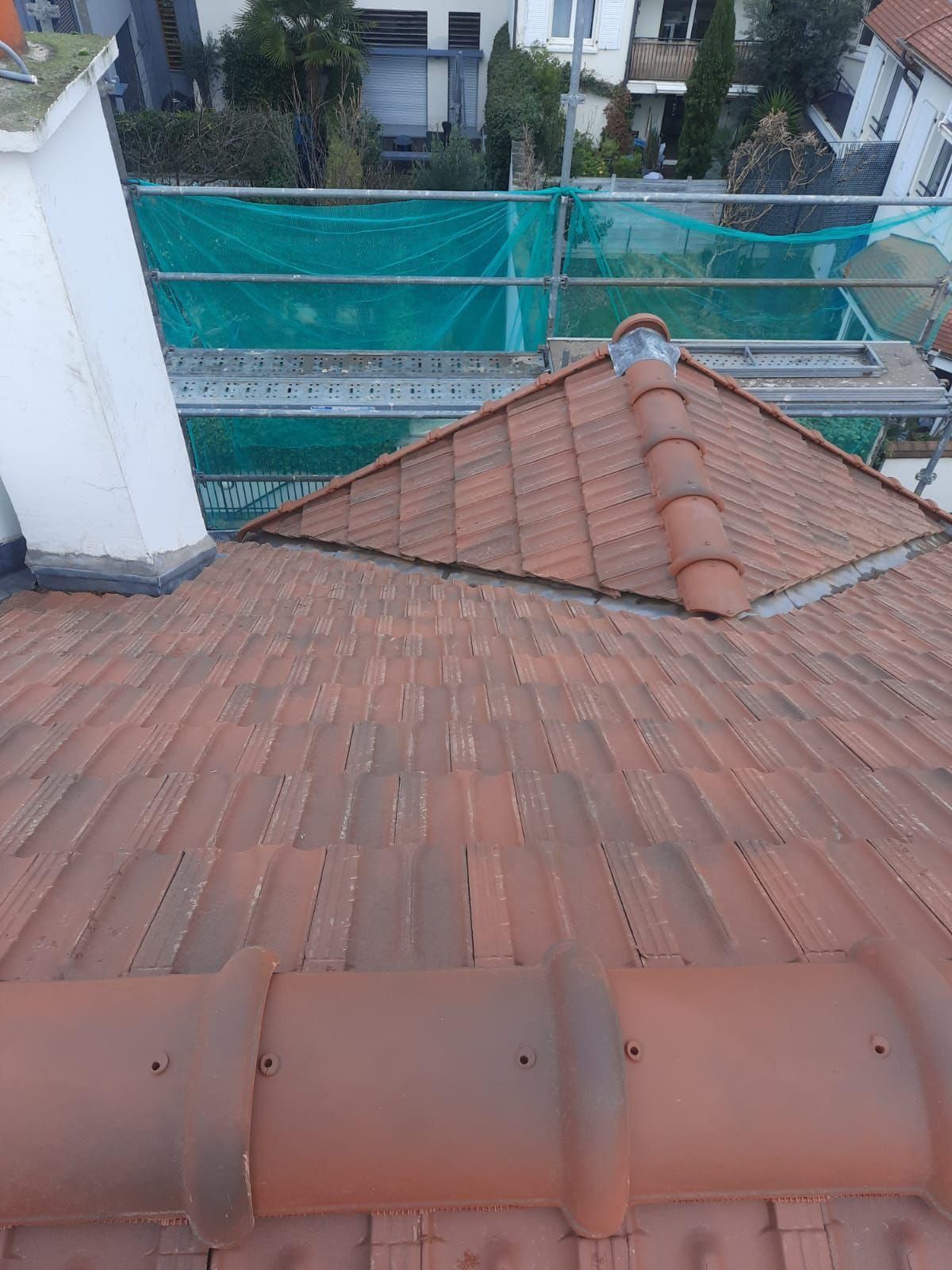 Toit en tuiles rouges avec cheminée, échafaudages et filets de sécurité.