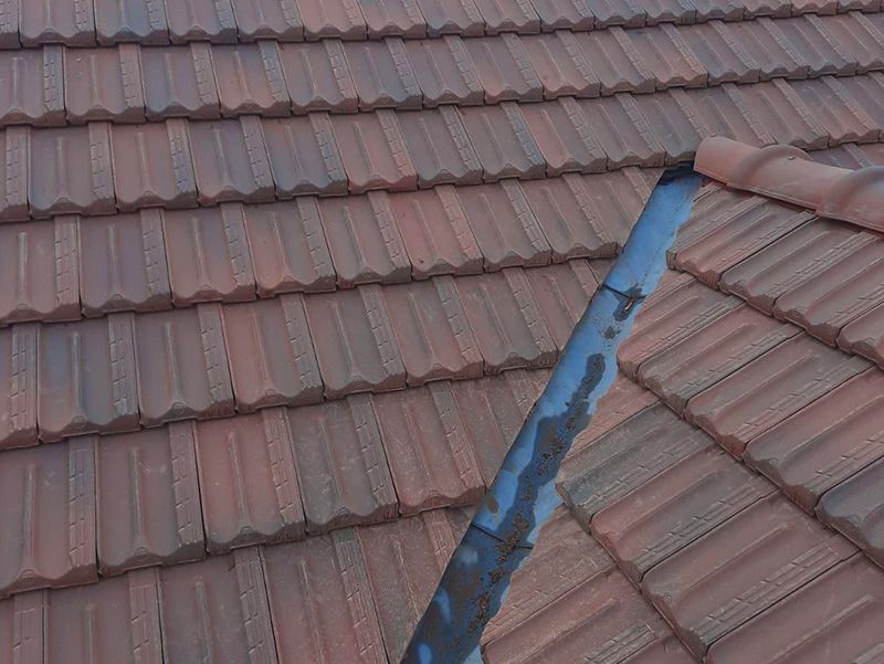 Toit en tuiles brunes avec un tuyau métallique qui s'élève vers le haut.