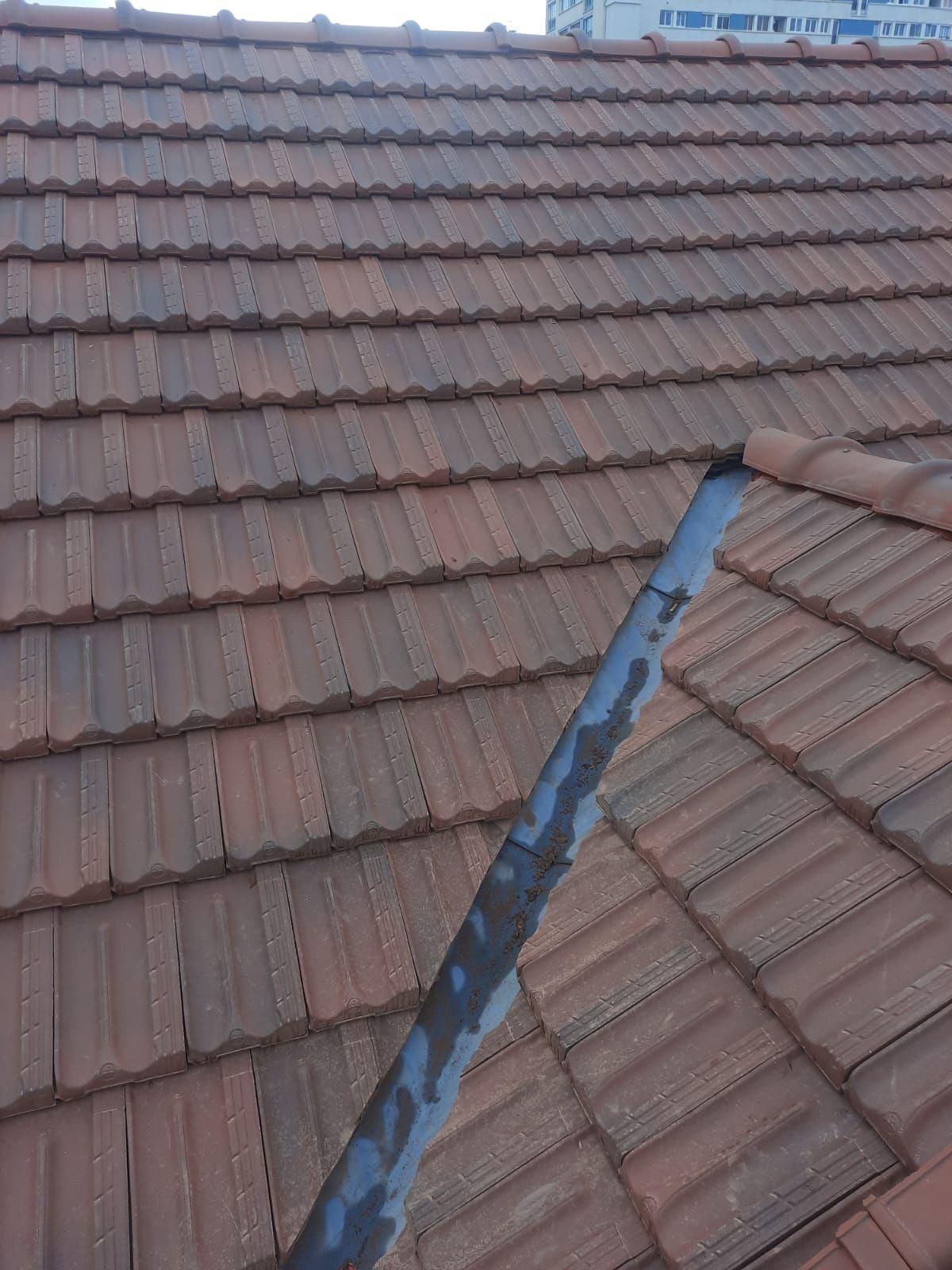 Toiture en tuiles de terre cuite avec un tuyau gris courant en diagonale.