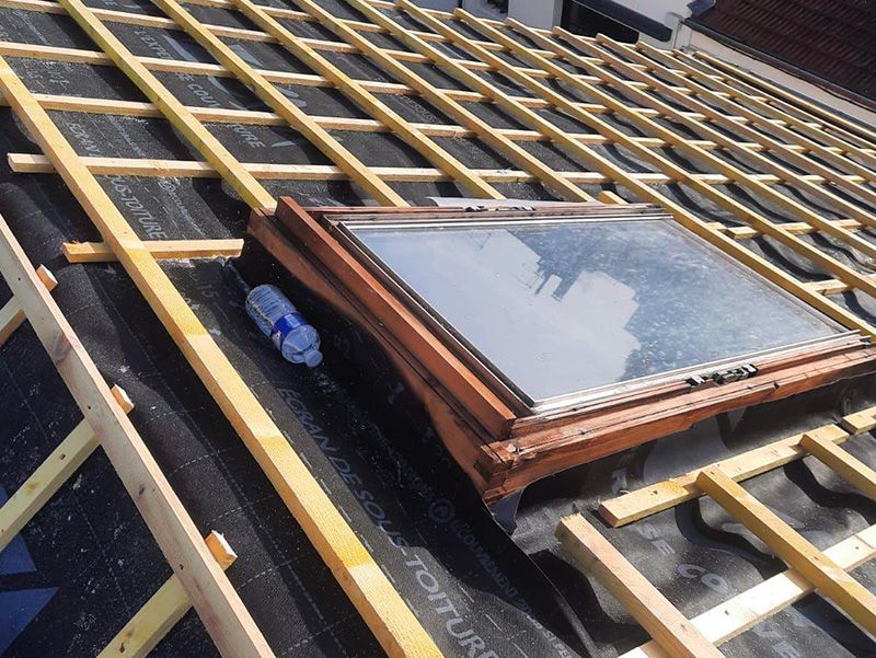 Toiture en construction avec puits de lumière, poutres en bois et sous-couche noire.