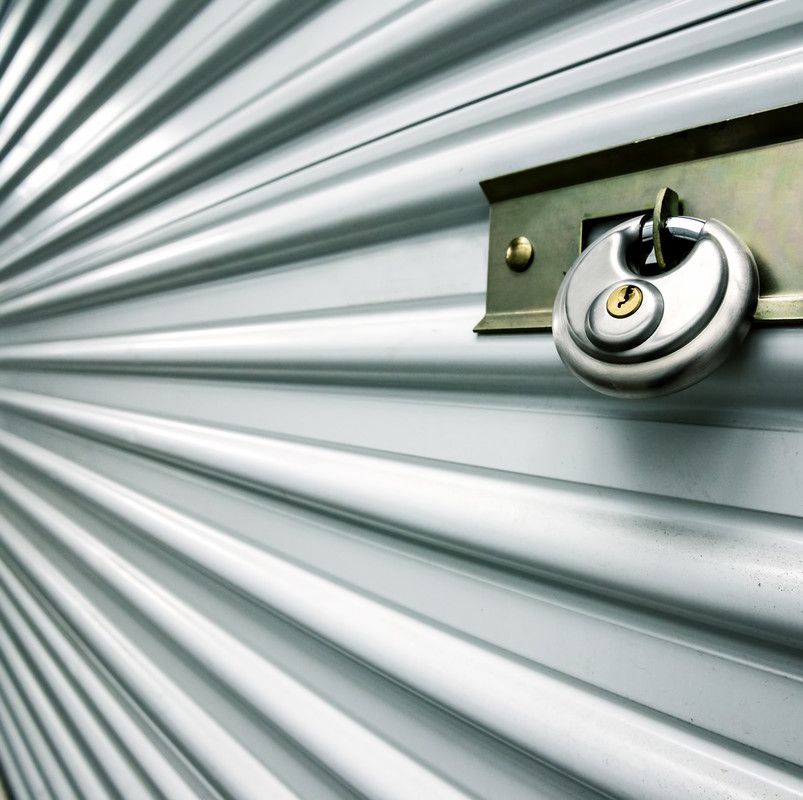 Un cadenas argenté sécurise la porte d'un box de stockage en tôle ondulée gris clair.