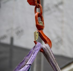 Crochet de grue rouge retenant une élingue violette et grise.