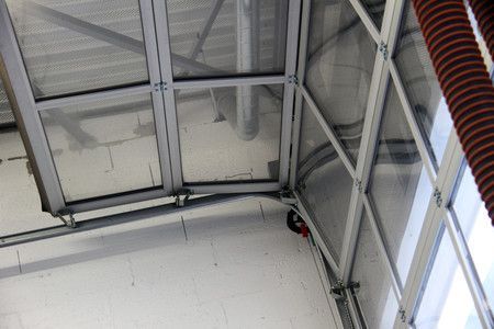 Vue intérieure d'un toit translucide et d'une structure métallique apparente. Le mur est blanc avec un angle en verre incurvé.