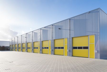 Rangée de bâtiments industriels aux portes de garage jaunes sous un ciel dégagé.