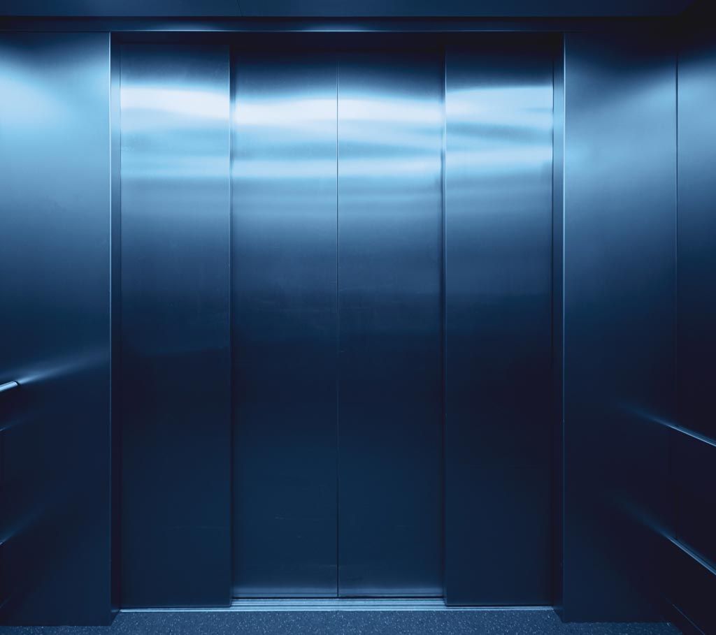 Vue intérieure d'un ascenseur en acier inoxydable, portes fermées, baigné d'une lumière bleue froide.