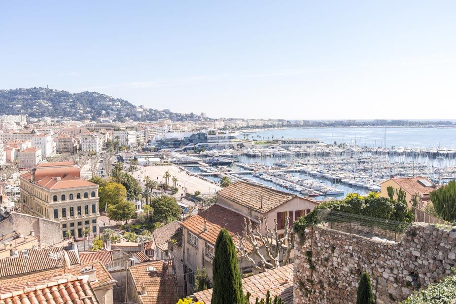 Cannes, France, paysage urbain avec marina, bâtiments aux toits de tuiles rouges et mer sous un ciel lumineux.
