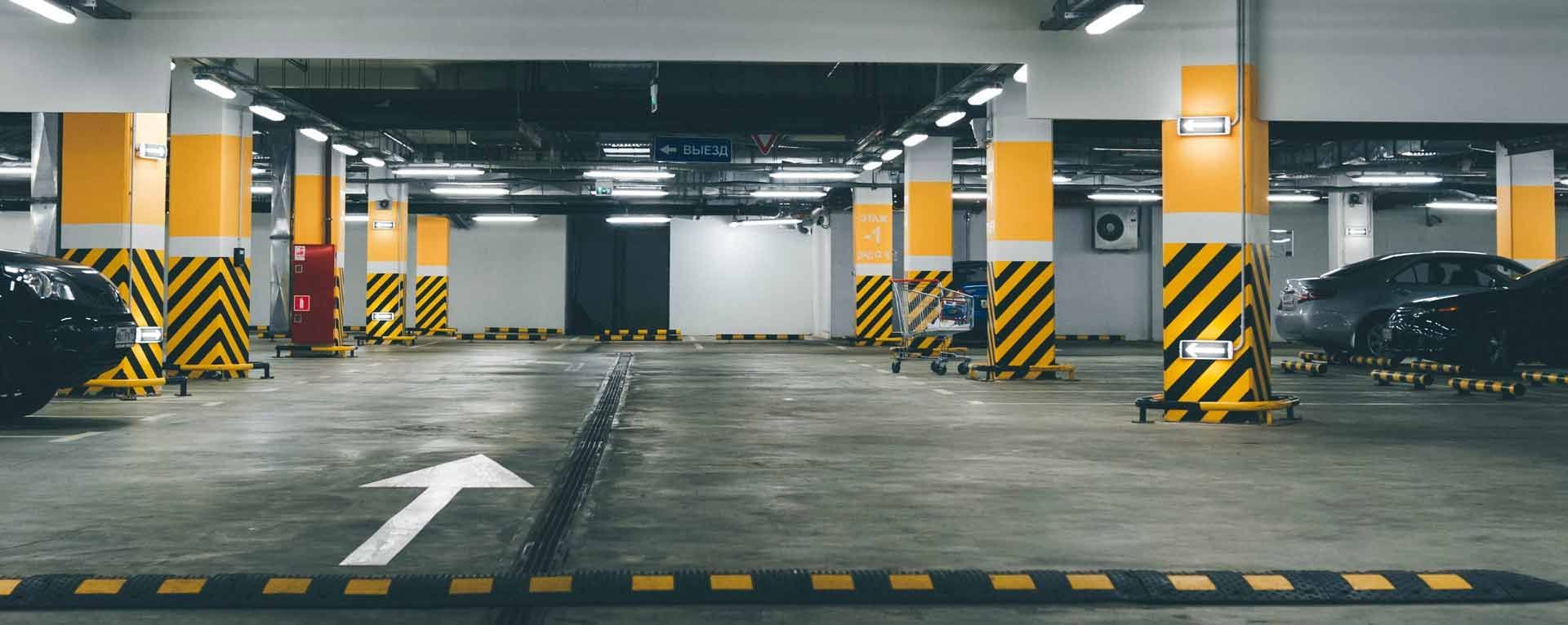 Parking souterrain avec des piliers de soutien rayés jaunes et noirs et une flèche pointant vers l'avant.
