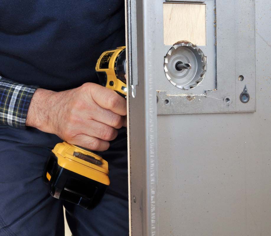 Une personne utilise une perceuse jaune pour installer une serrure sur une porte métallique.