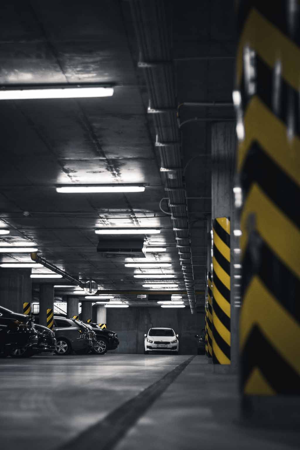 Parking souterrain avec voitures, pilier de soutien à rayures jaunes et noires et éclairage zénithal.