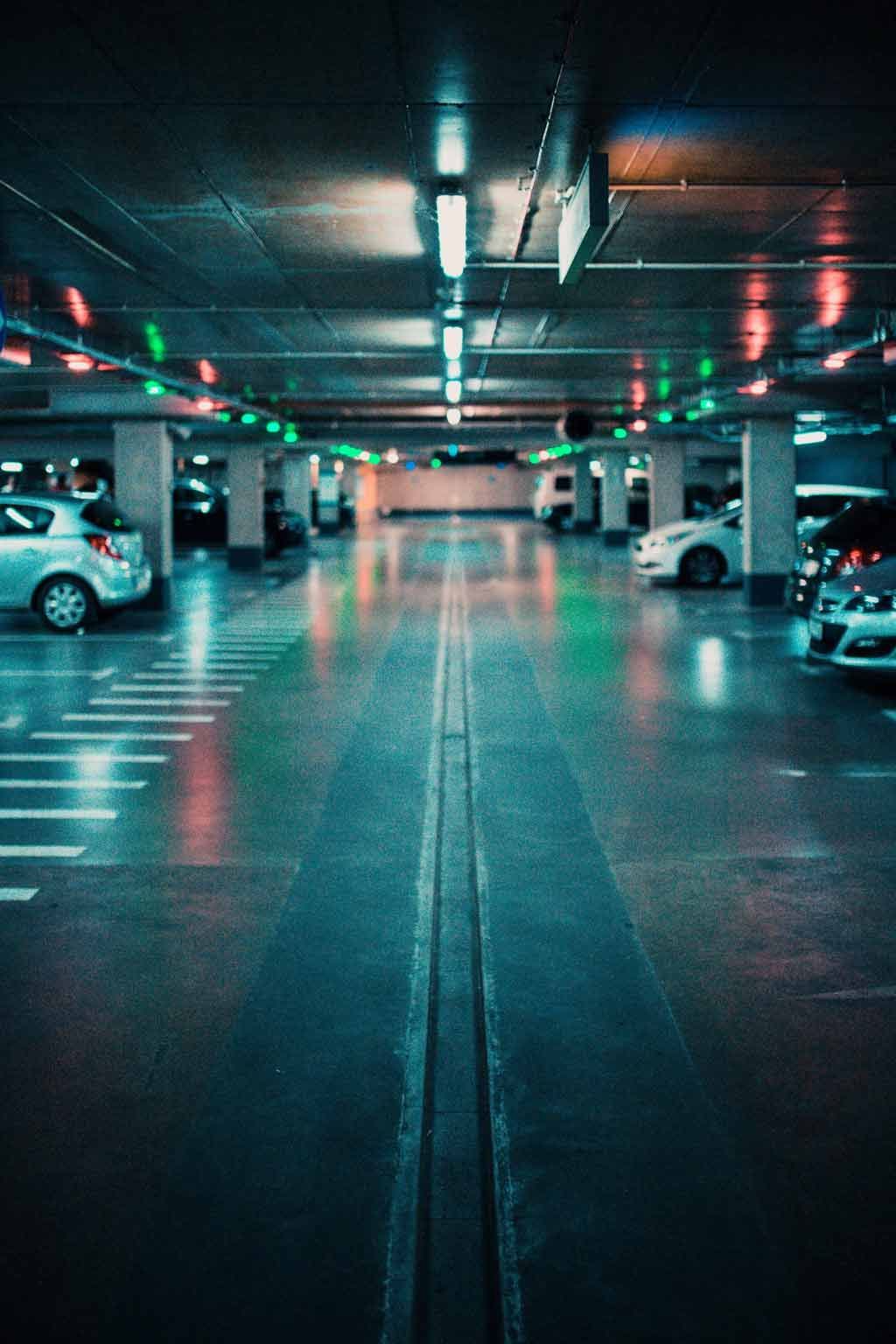 Parking souterrain vide et faiblement éclairé, avec des rangées de voitures et des plafonniers.
