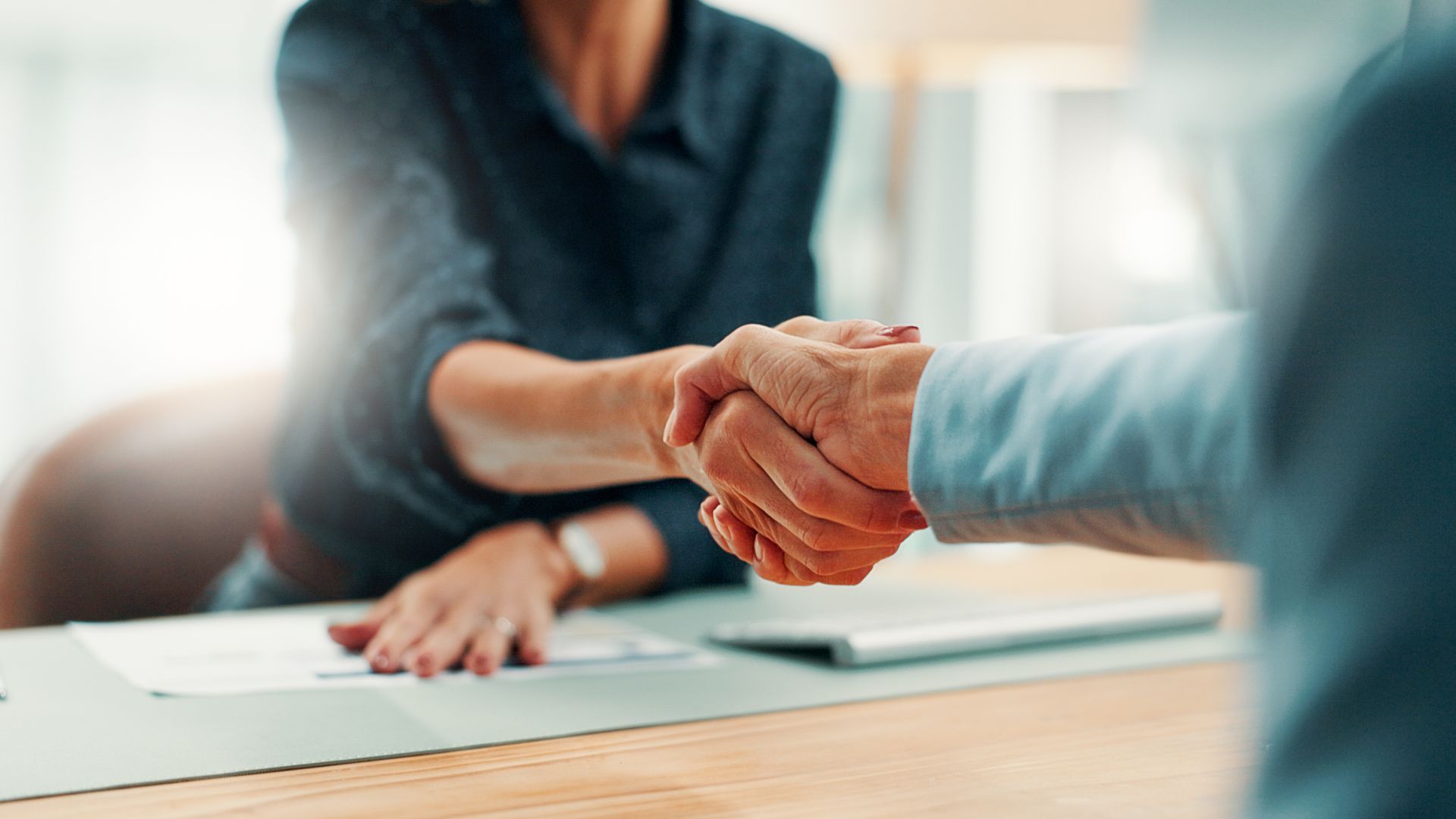 Deux personnes se serrent la main par-dessus un bureau dans un bureau lumineux