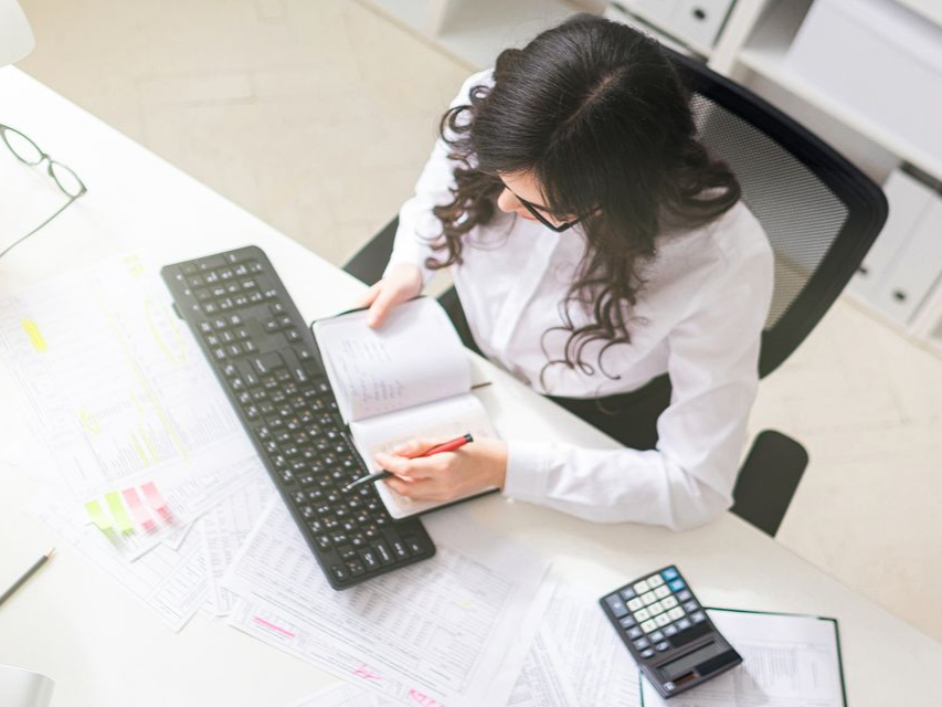 Une femme travaille à un bureau avec un clavier, un ordinateur portable et une calculatrice dans un bureau lumineux.