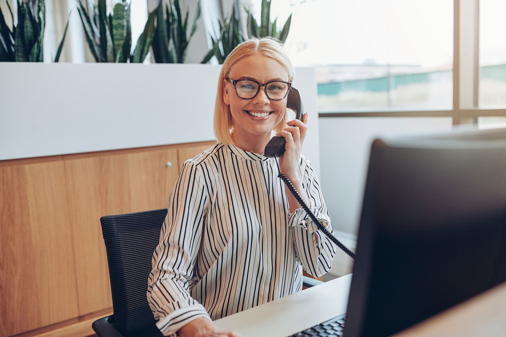 Une employée souriant au téléphone, assis à son bureau dans un bureau lumineux