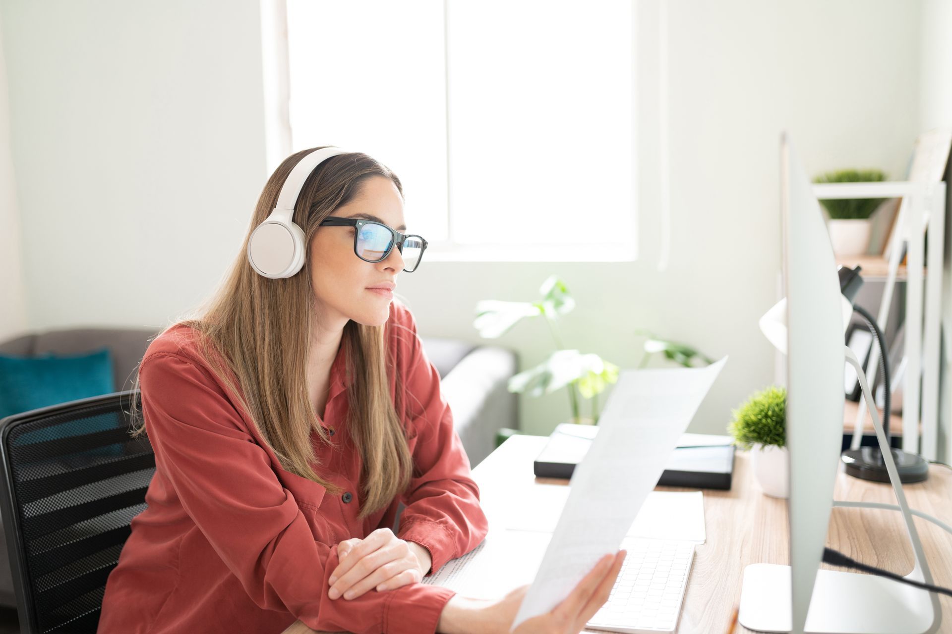Une femme portant un casque et des lunettes travaille sur un ordinateur portable dans un bureau à domicile lumineux