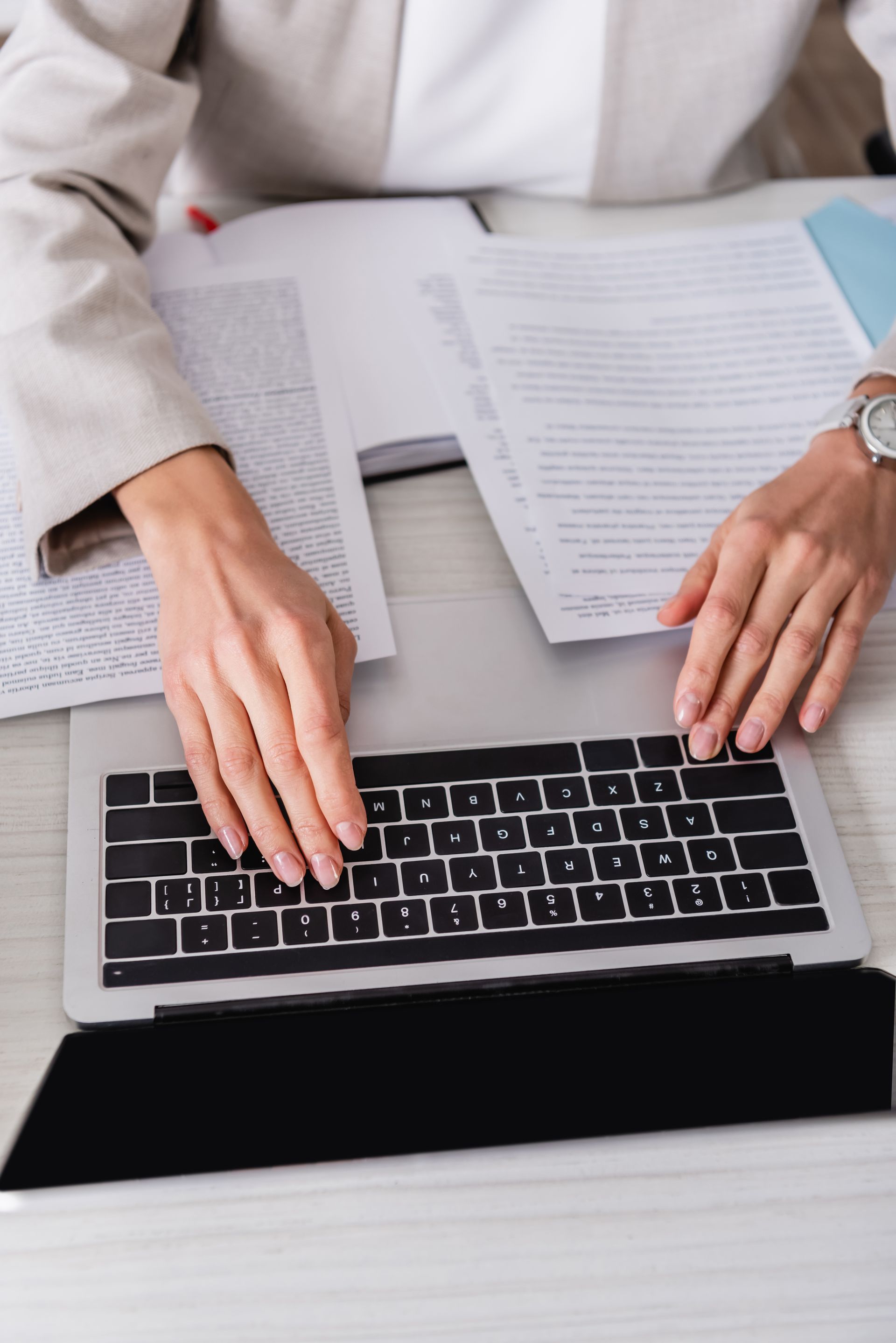 Des mains tapent sur un ordinateur portable à côté de papiers et de documents posés sur un bureau.