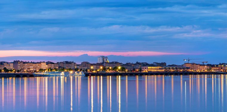 La silhouette de la ville au crépuscule se reflète sur l'eau calme, offrant un spectacle coloré.