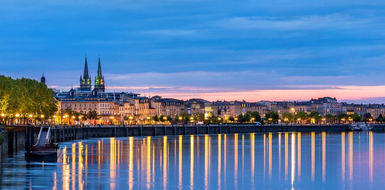 Vue de la ville au crépuscule, avec les flèches des cathédrales, les lumières scintillantes et les reflets sur l'eau calme.