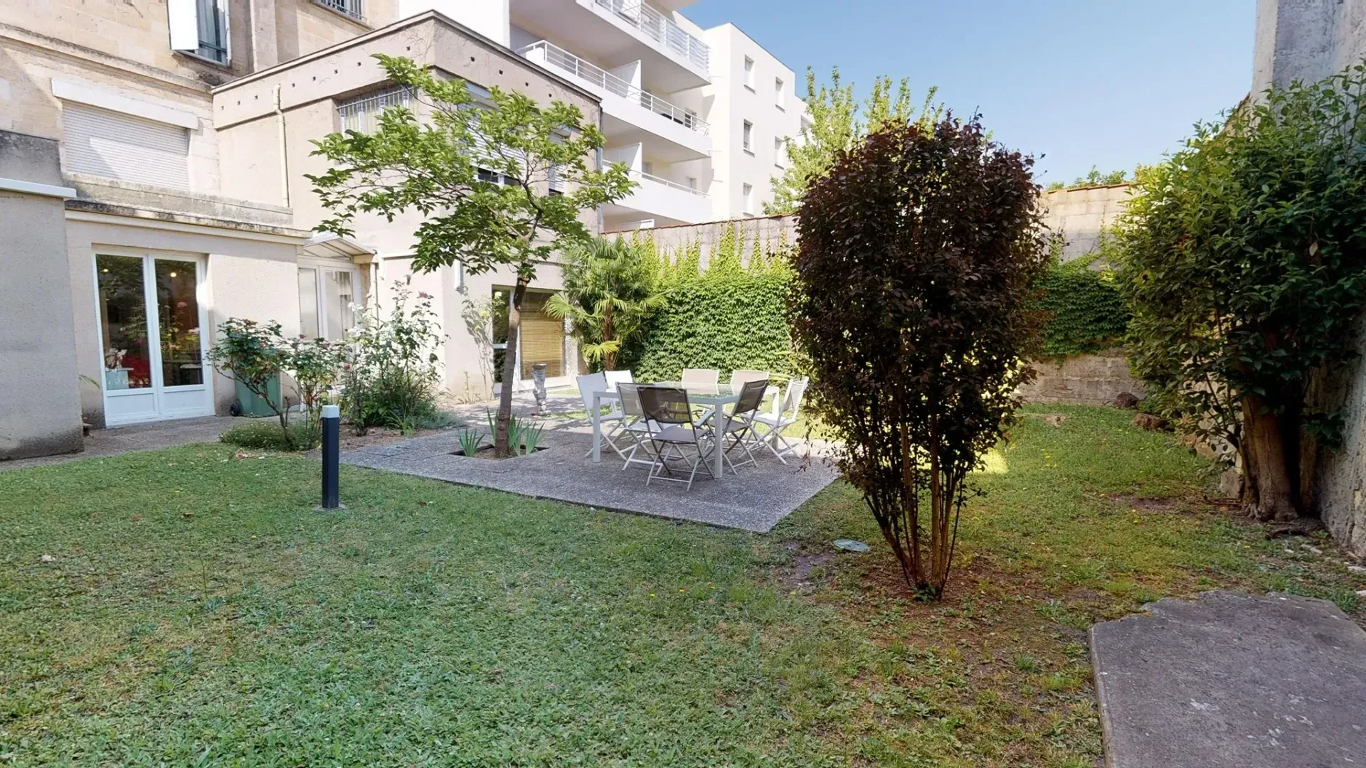 Petit jardin intérieur avec pelouse, arbres, terrasse et immeubles d'appartements en arrière-plan.