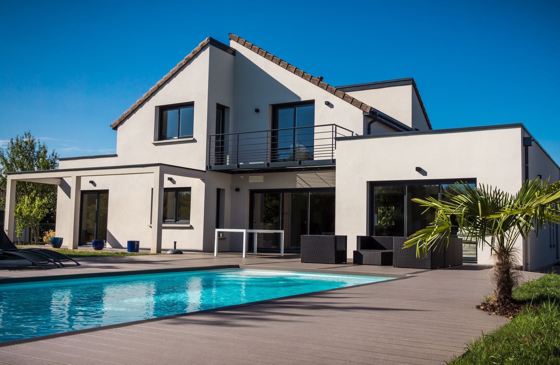 Une maison moderne à deux étages avec piscine, mobilier de terrasse et un ciel bleu azur en arrière-plan.