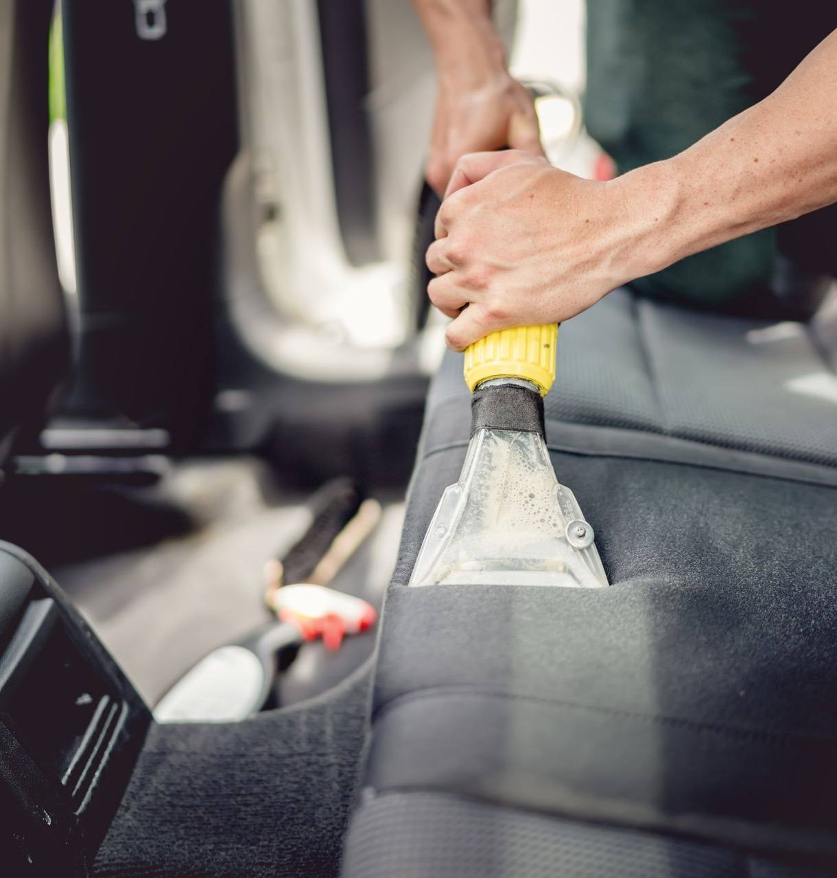 Une personne utilise une machine de nettoyage pour aspirer un siège auto.