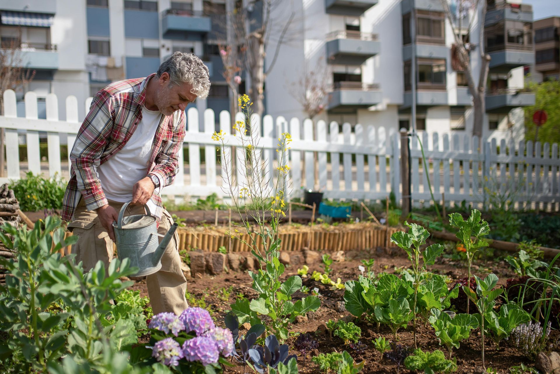 Ein Mann bewässert einen Garten mit einer Gießkanne aus Metall