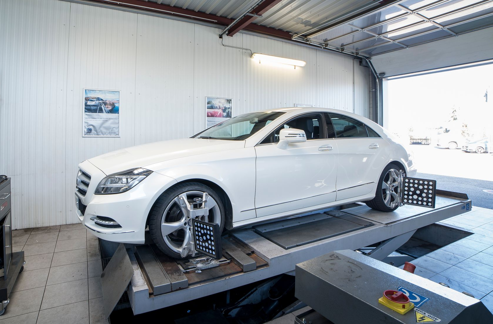 Mercedes blanche sur un pont élévateur dans l'atelier, en cours de réglage de la géométrie.