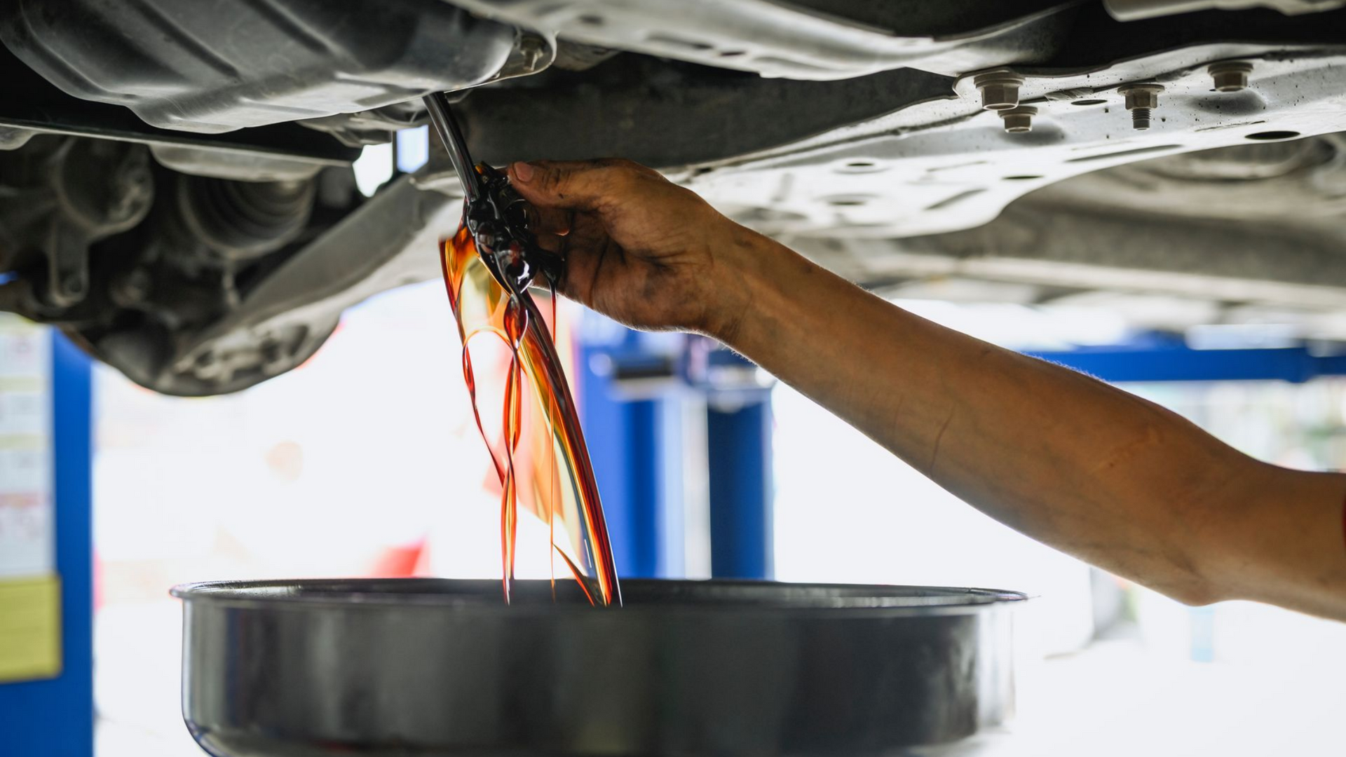 Garagiste qui vide l'huile d'un véhicule dans un récipient.