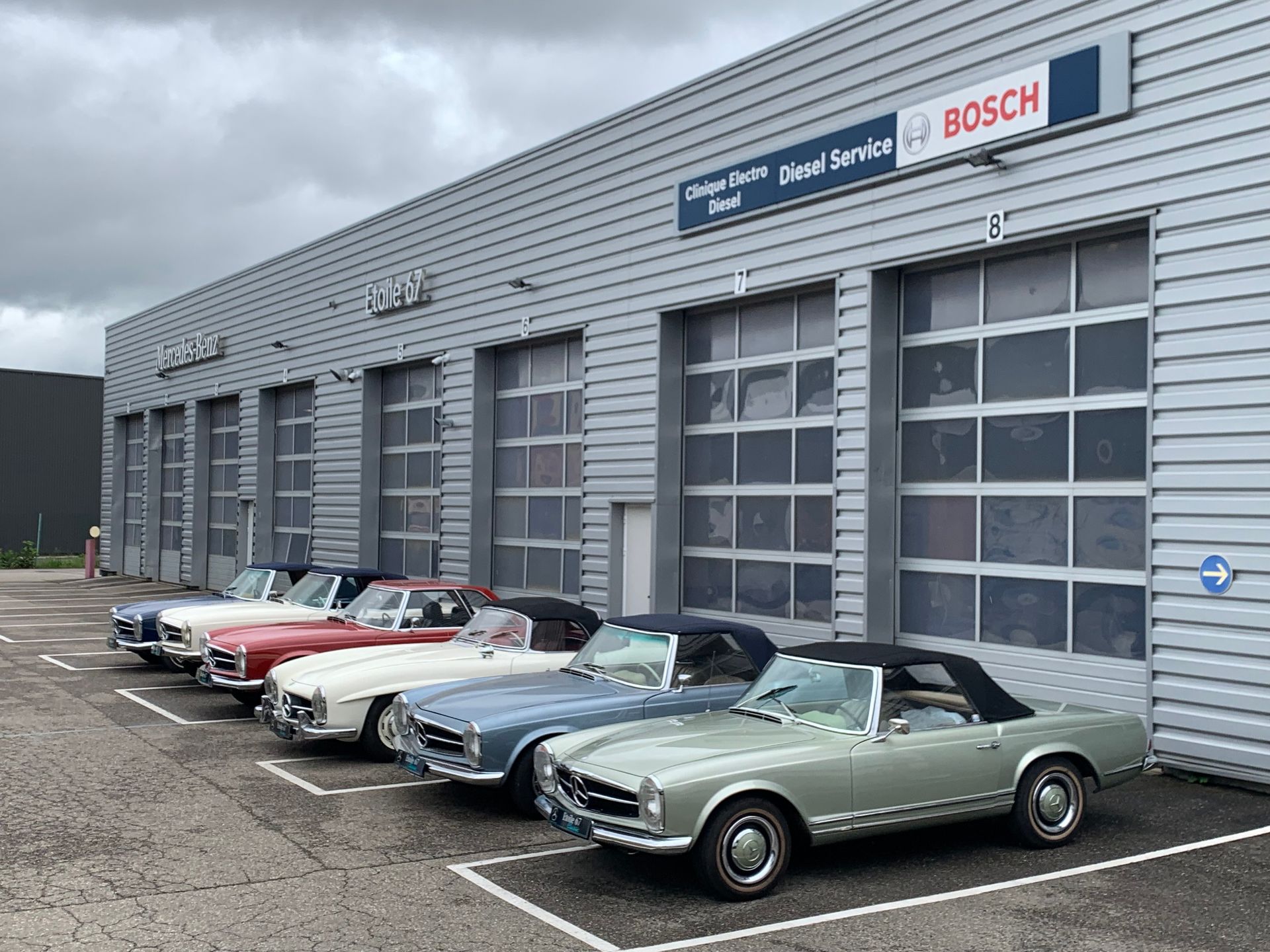 Des cabriolets classiques garés devant un garage automobile gris avec une enseigne BOSCH.