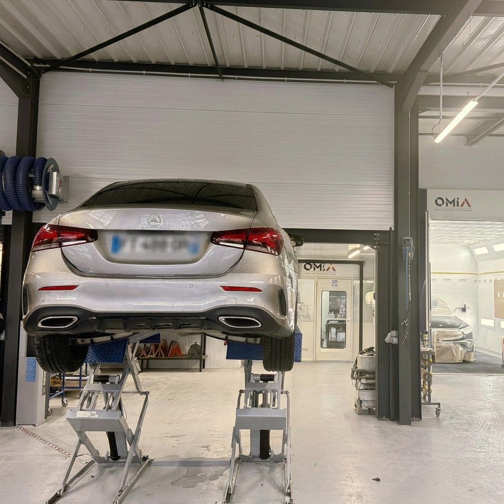 Berline argentée soulevée sur un pont élévateur à l'intérieur de l'atelier de réparation du garage.