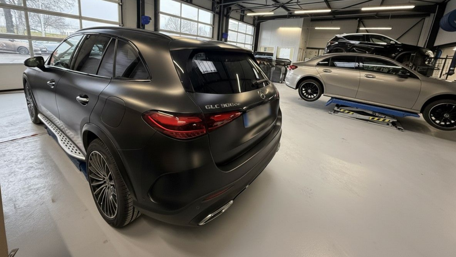 Une berline Mercedes noire dans un garage, à côté d'une voiture argentée sur un pont élévateur.