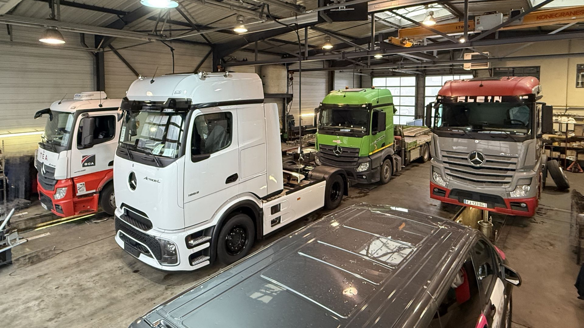 Des camions à l'intérieur d'un garage, dont un camion à cabine blanche, verte, rouge et grise.