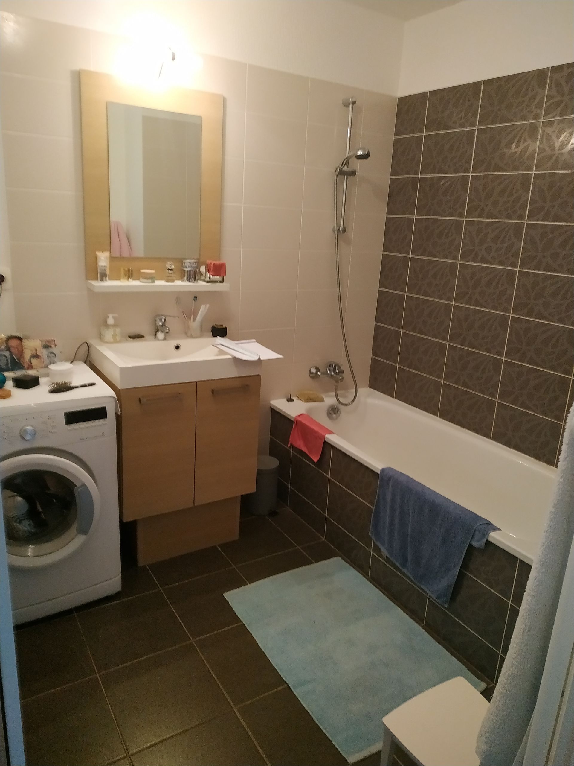 Salle de bain avec machine à laver, lavabo, baignoire et carrelage marron et beige.