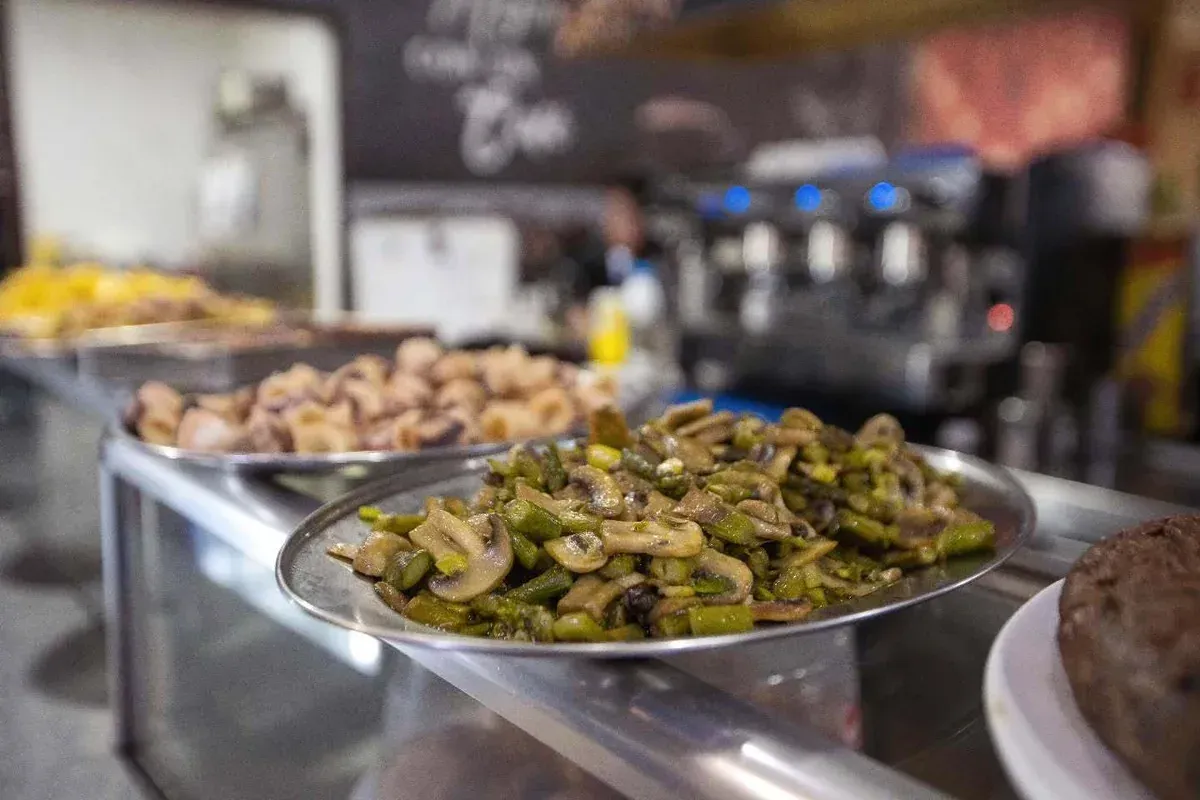 Mostrador de buffet con bandejas de verduras cocinadas y otros platos en la cocina de un restaurante.