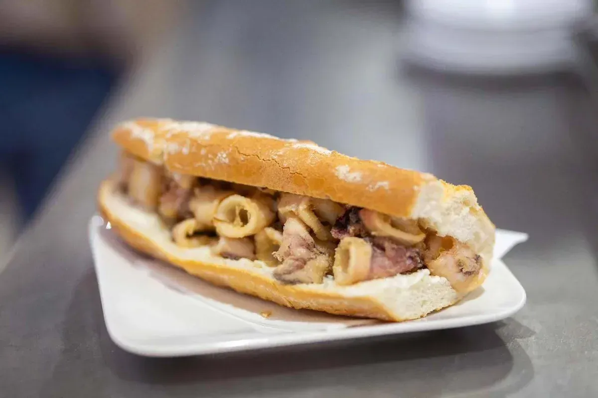 Un sándwich con carne en rodajas y cebolla en un plato blanco sobre una mesa.