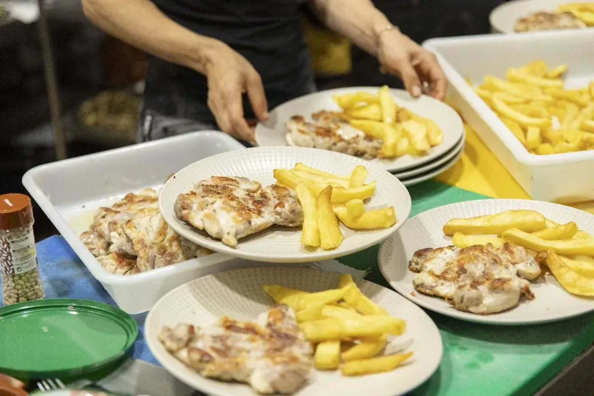 Platos de pollo a la parrilla y papas fritas servidos en una mesa por las manos de un cocinero.