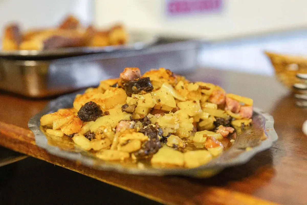 Plato de pasta con salsa de carne sobre una mesa de madera, con una bandeja de comida desenfocada al fondo.