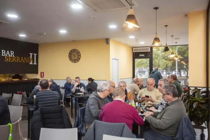 Gente cenando y charlando dentro de un bar acogedor con iluminación cálida y decoración en las paredes.