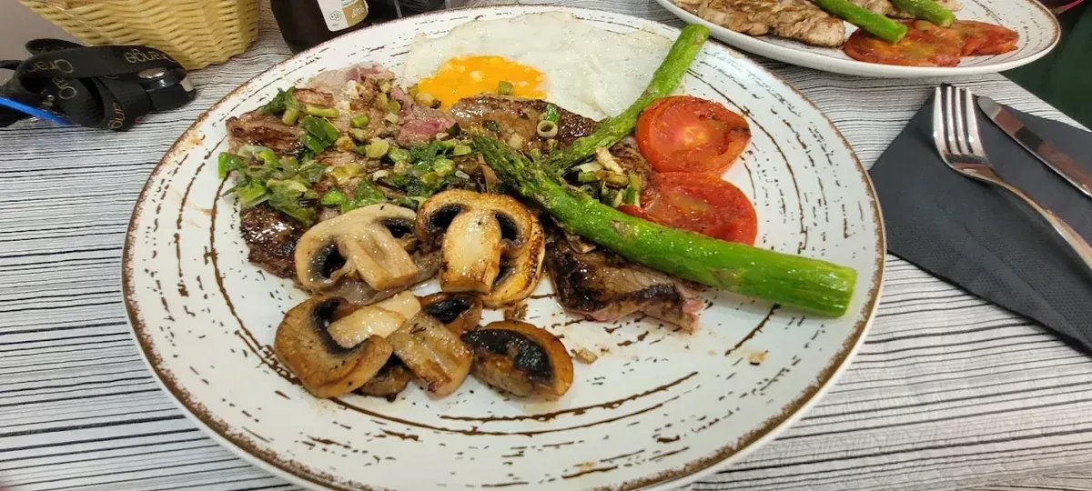 Espárragos a la parrilla, champiñones, rodajas de tomate y un huevo frito en un plato blanco en una mesa de comedor.