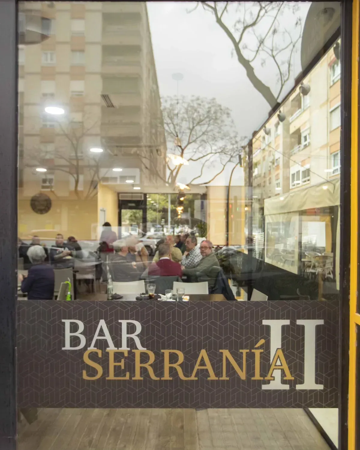 Fachada del Bar Serranía con gente sentada en una luminosa terraza de cafetería.