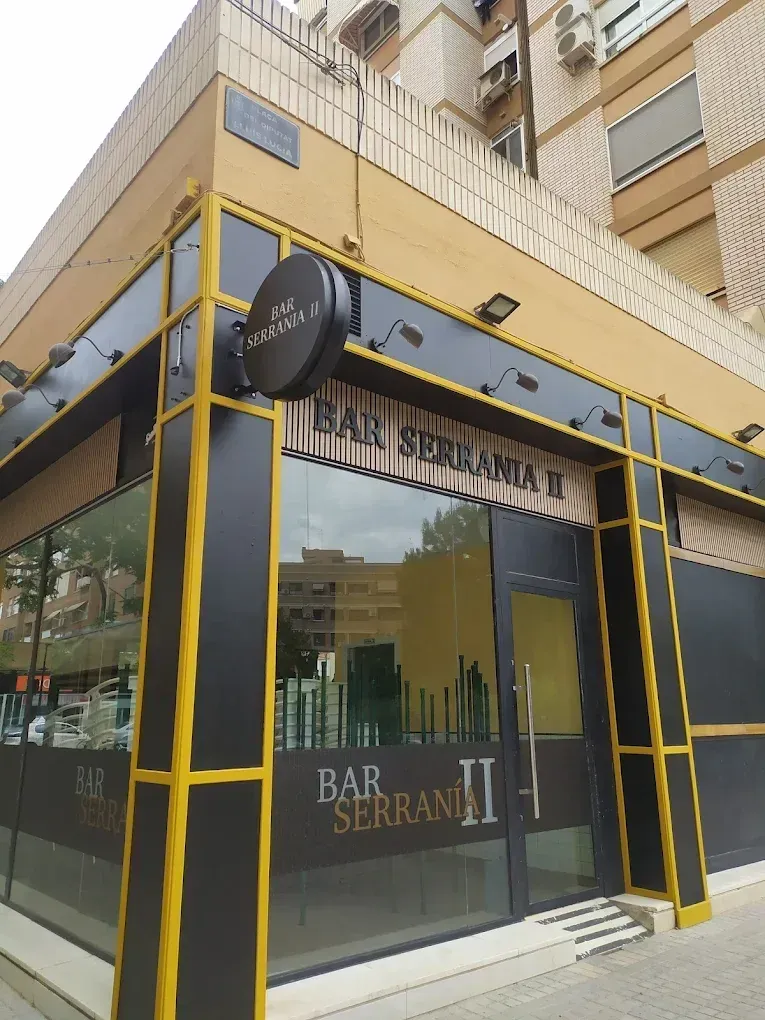 Fachada de una barbería con detalles en negro y amarillo y ventanas de cristal en un edificio de la ciudad.