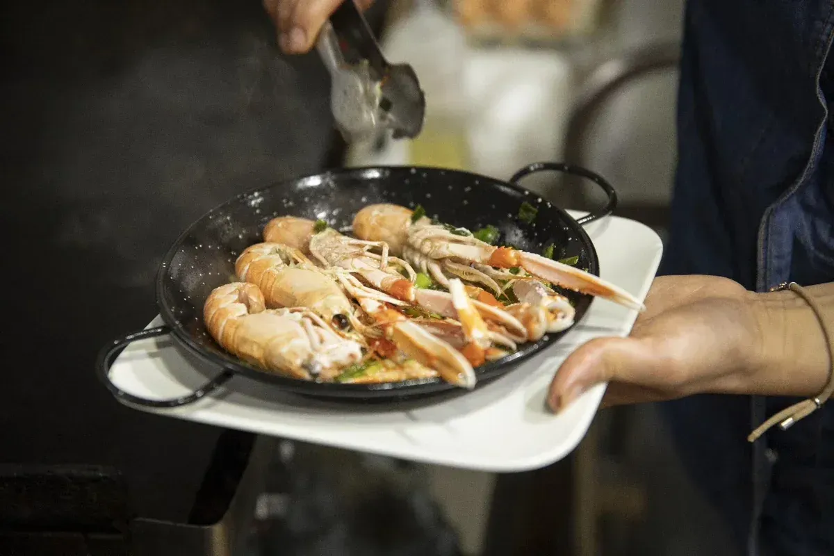 Manos sirviendo camarones a la parrilla en una fuente blanca en una mesa ahumada.