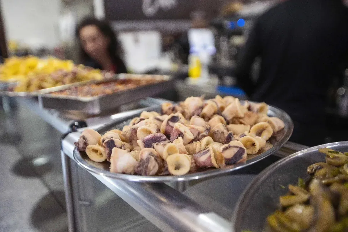 Bandejas con pasteles y aperitivos variados sobre una mesa de bufé, con personas difuminadas al fondo.